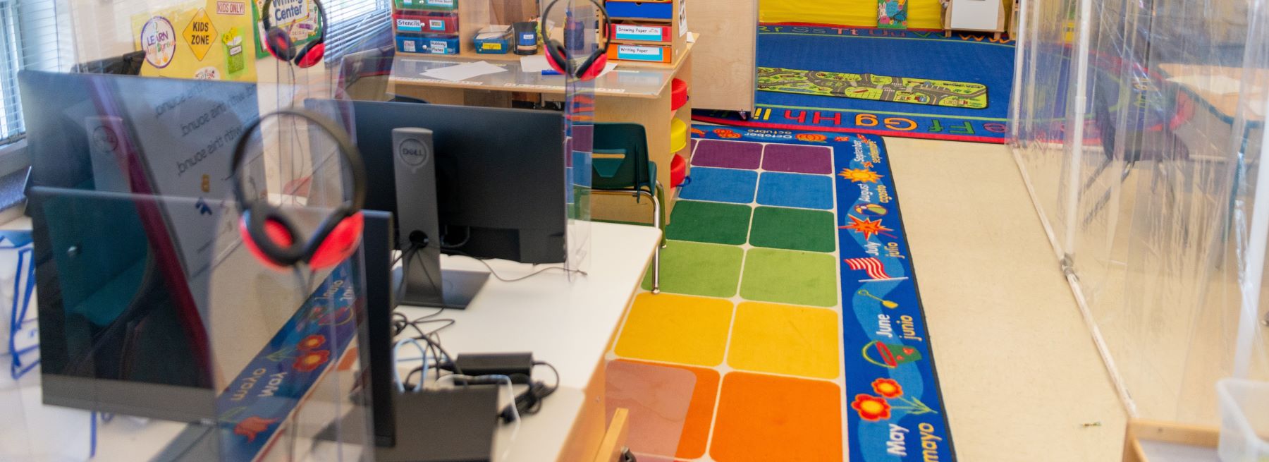 A vibrant classroom with a colorful carpet and an computers on tables for students..