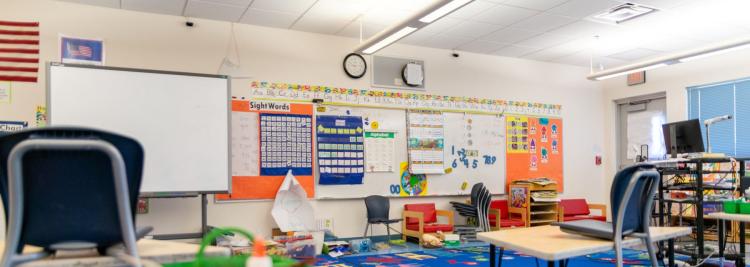empty classroom with desks, colorful projects on board and two clocks on the wall